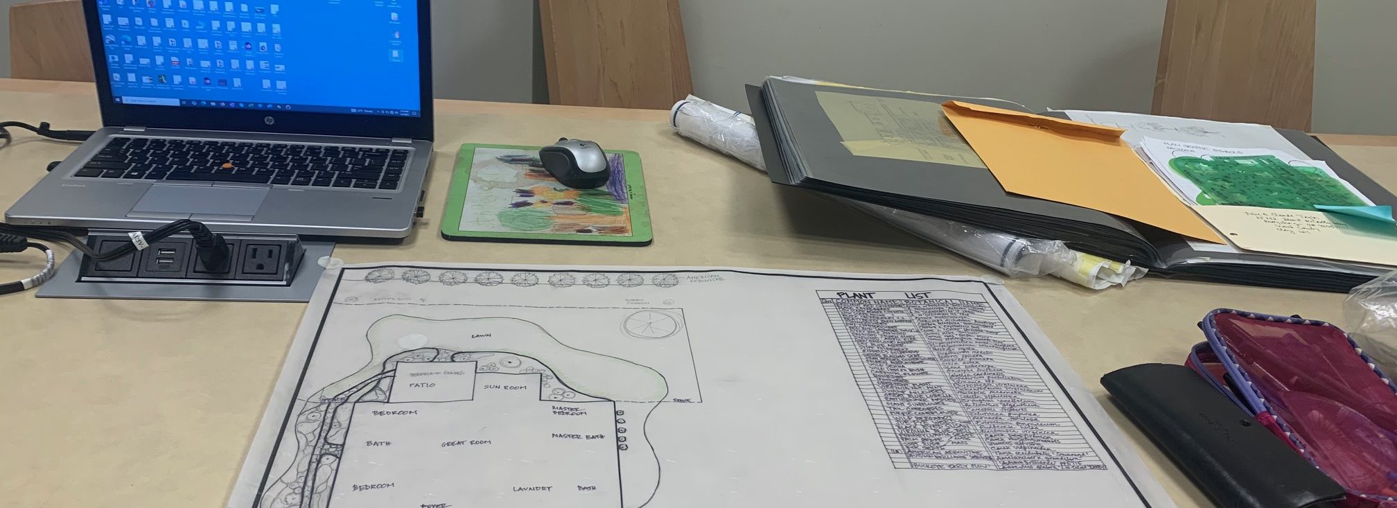 Landscape design consultation table with a site plan, plant list, and laptop